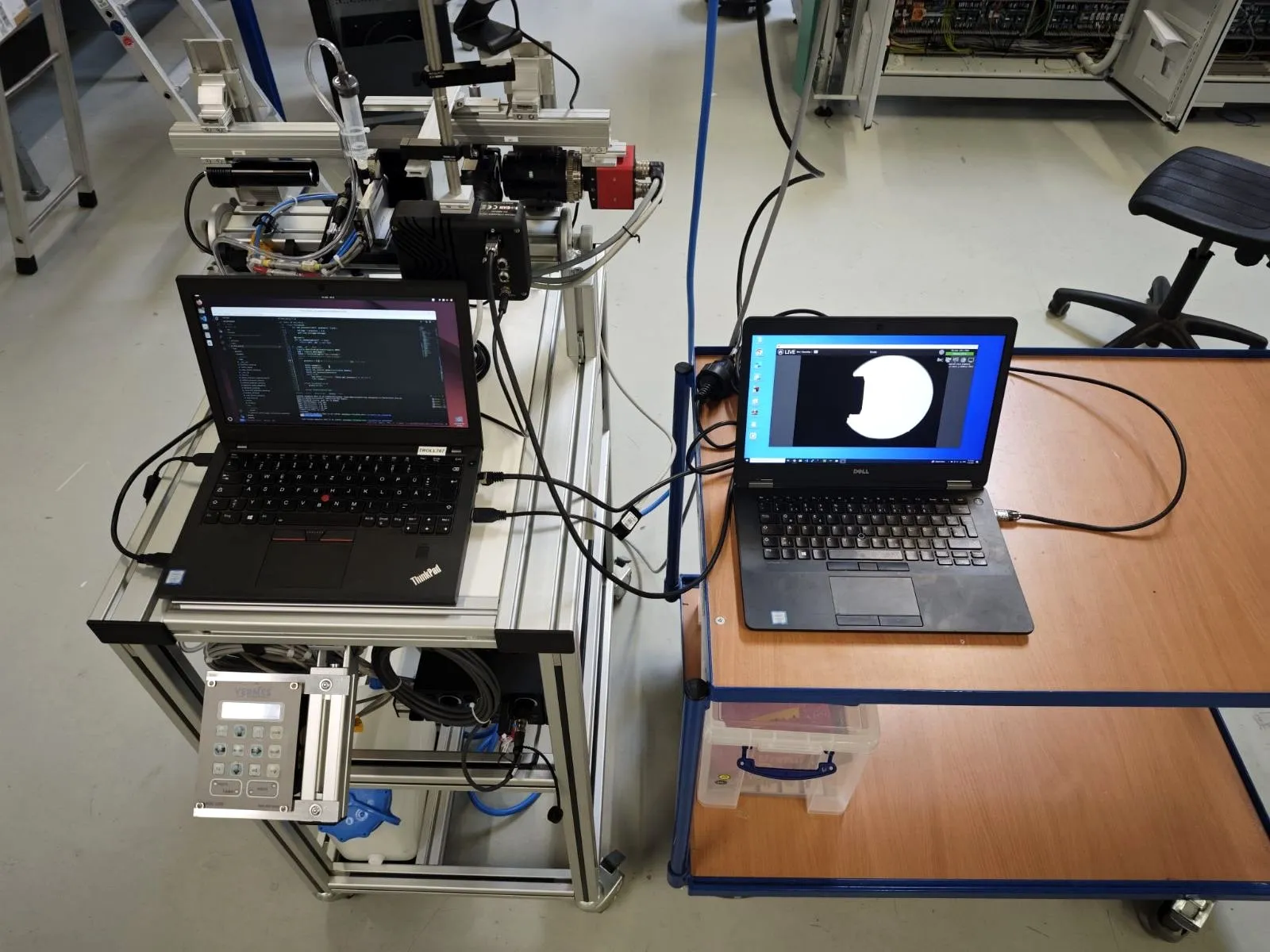 A laptop screen showing a live, high-contrast silhouette of a single paint droplet captured by the camera rig beside it.